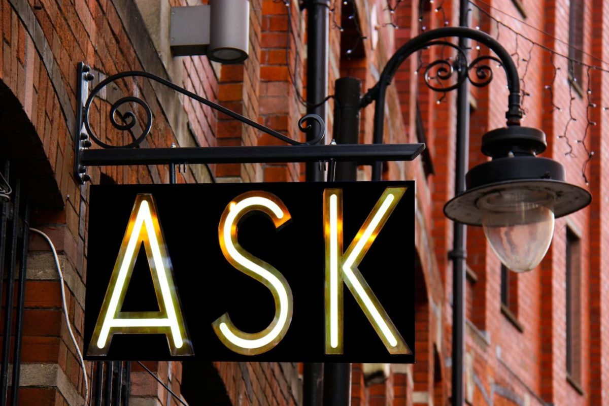 An ornate hanging store sign with "ASK" in neon