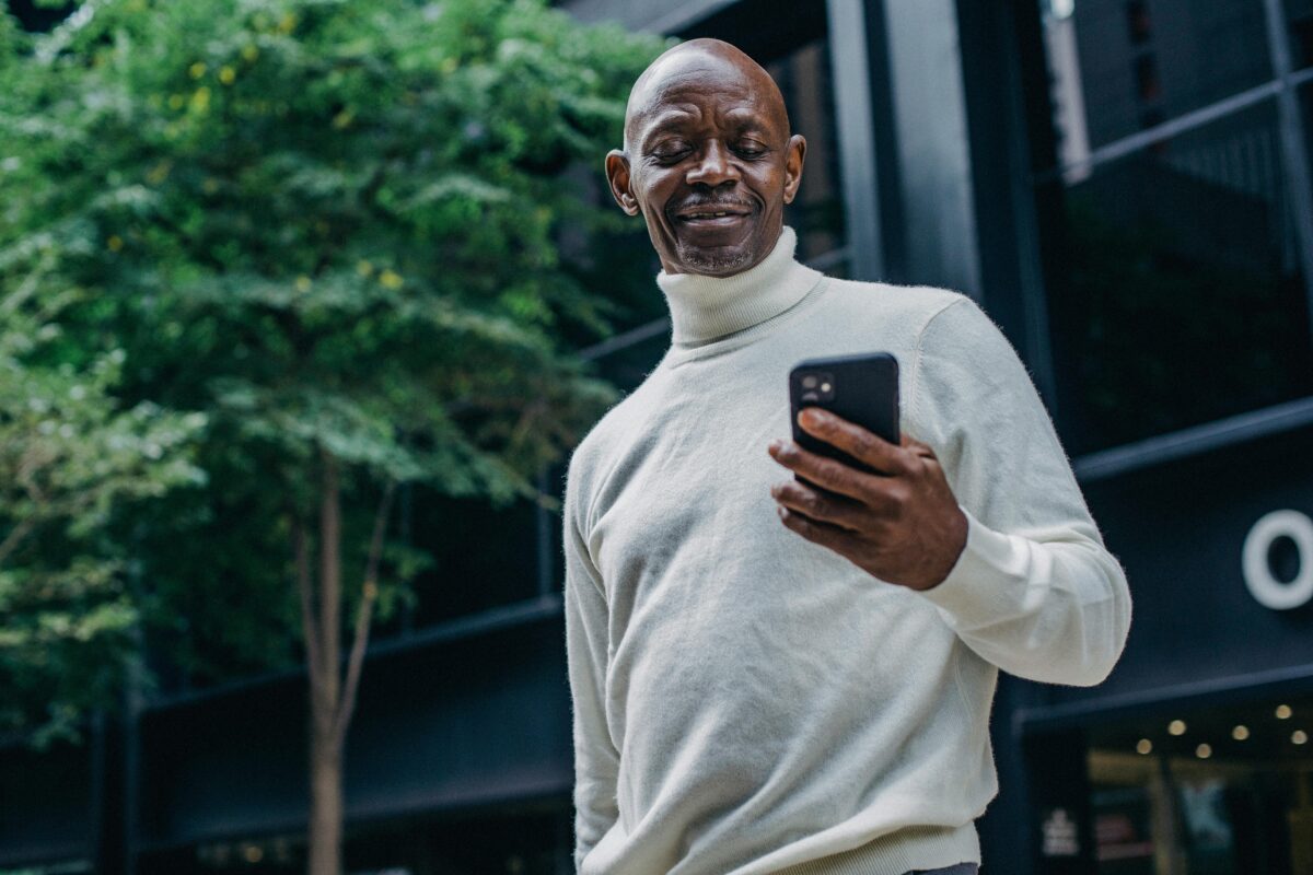 Photo fo a bald, middle-aged Black man smiling into his phone. Photo by Ono Kosuki via Pixels.