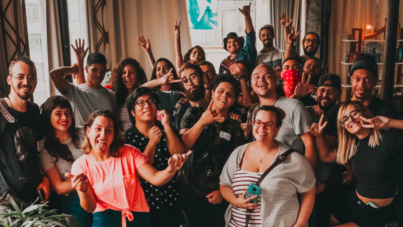 Group of multiethnic, multiracial young adults in a group, smiling, raising their hangs in triumph.